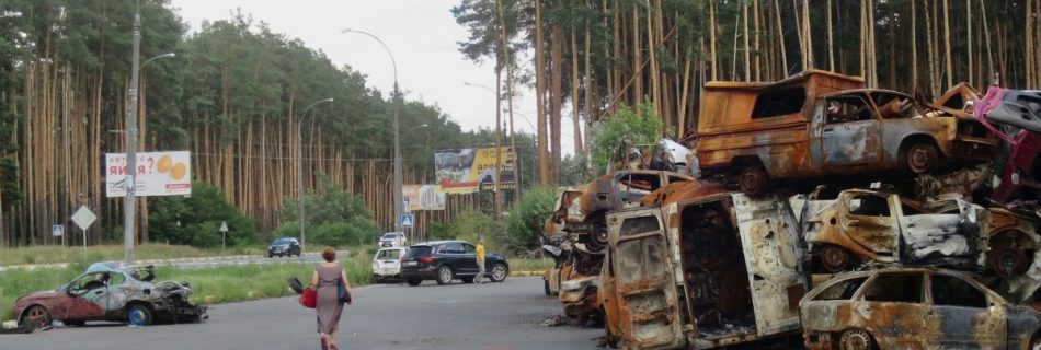 a street in ukrain with a woman walking past a pile of destroyed cars